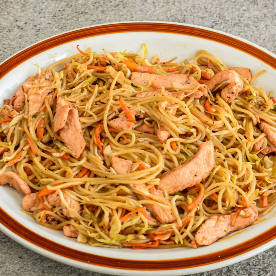 Nepalese chicken chowmein with noodles, chicken strips, carrots, and cabbage on a white plate.