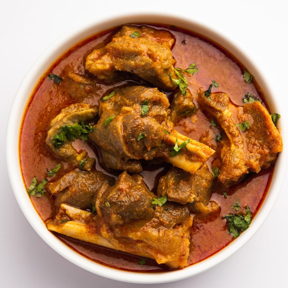 Close-up of a bowl of Nepalese mutton curry with bone-in meat and fresh cilantro.